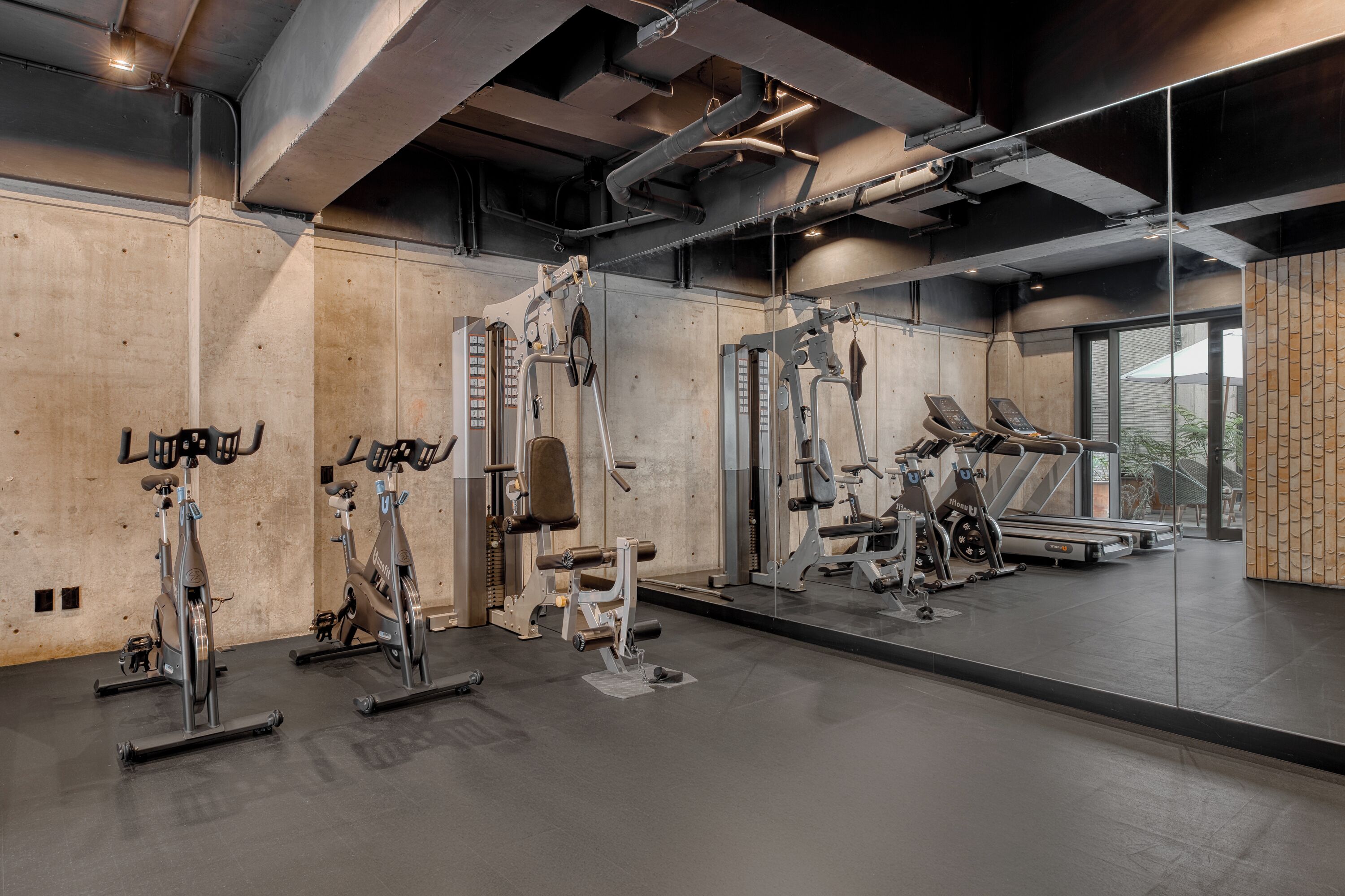A gym with exercise equipment, a large mirror, and a concrete wall.
