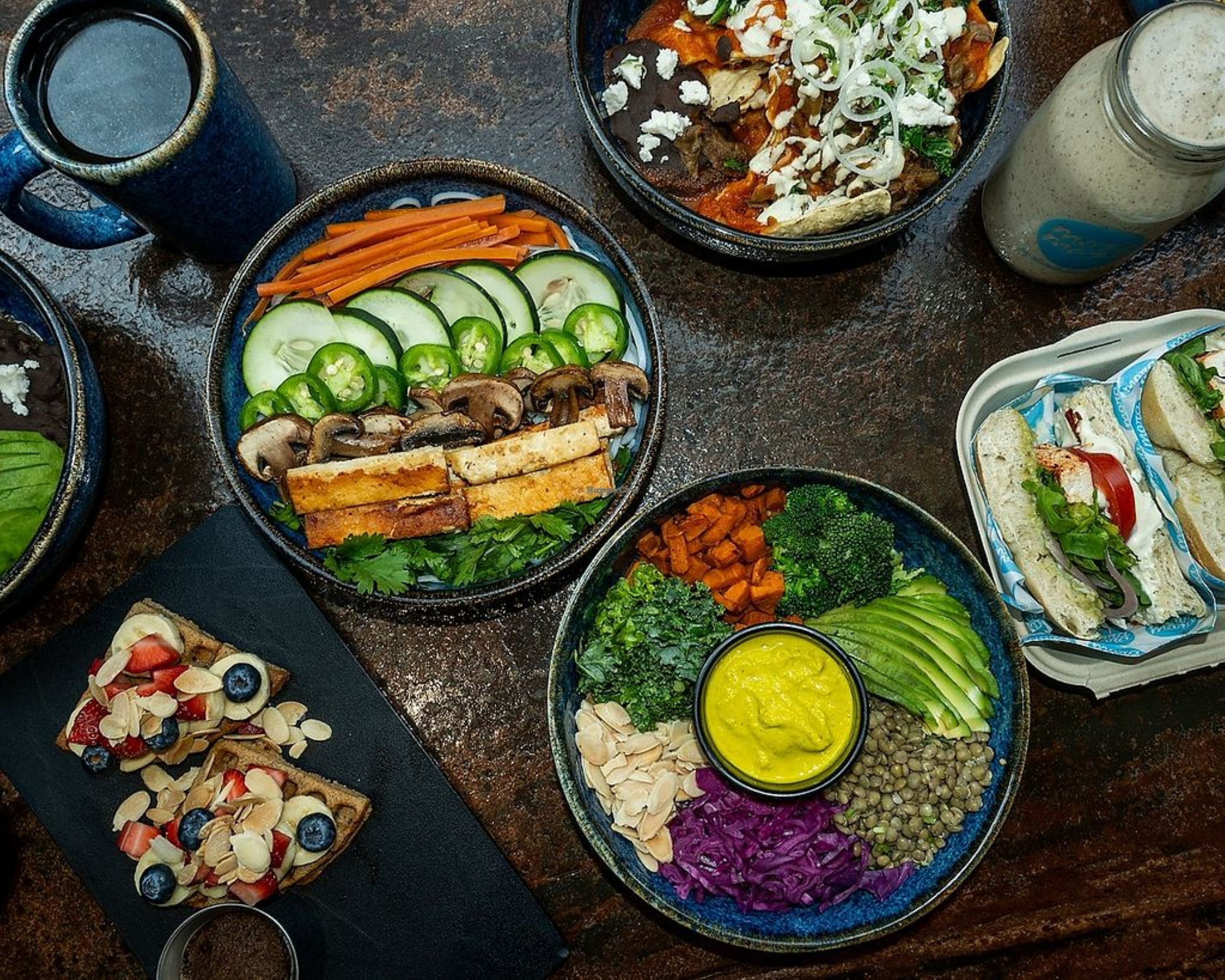 A variety of dishes including a salad with cucumbers, mushrooms, and carrots, a bowl of hummus, and sandwiches.