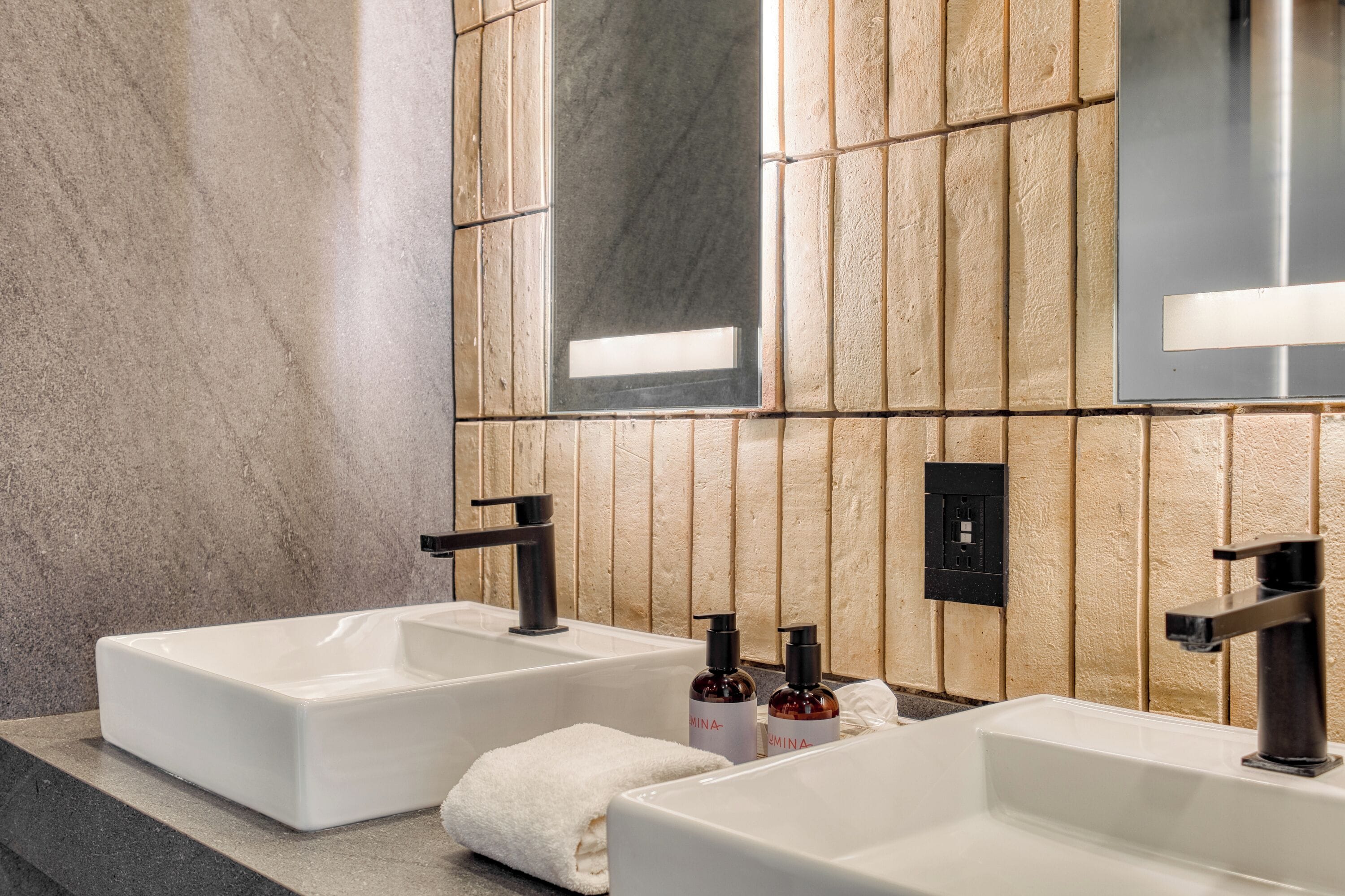 A bathroom with two white sinks, black faucets, and a wooden wall paneling.