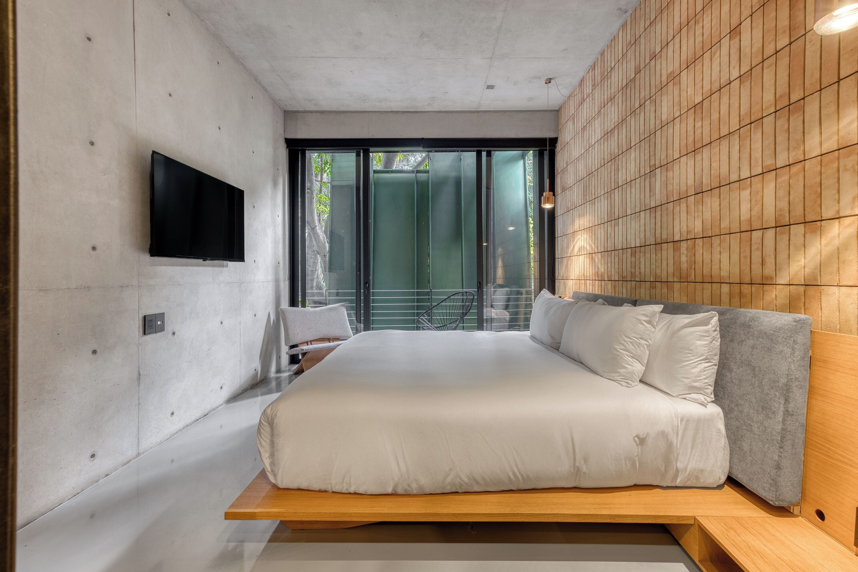 Une chambre à coucher moderne, dotée d’un grand lit, d’un téléviseur fixé au mur et offrant une vue sur l’extérieur grâce à de grandes fenêtres.