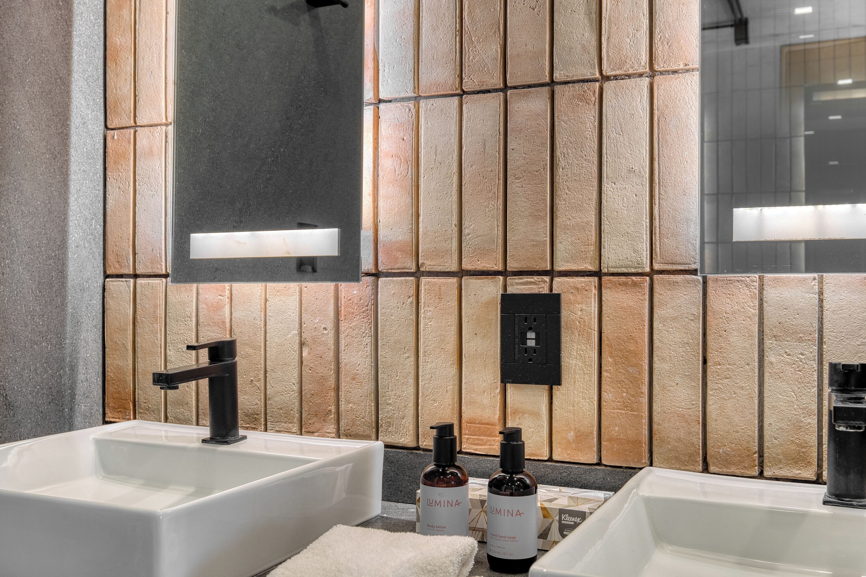 A modern bathroom with two sinks, a large mirror, and a textured wall.
