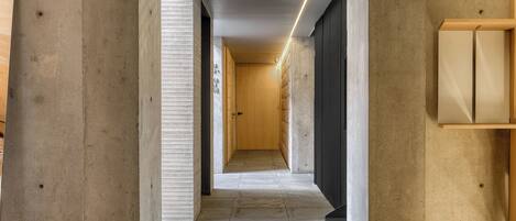 A narrow hallway with a wooden door at the end, tiled floor, and a light strip along the ceiling.