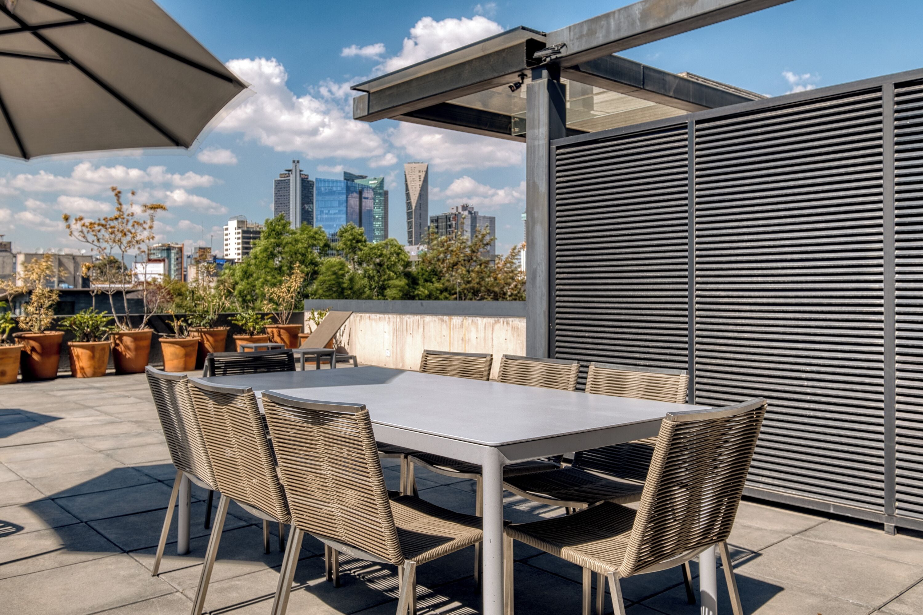 An outdoor patio with a table and chairs, potted plants, and a city skyline in the background.