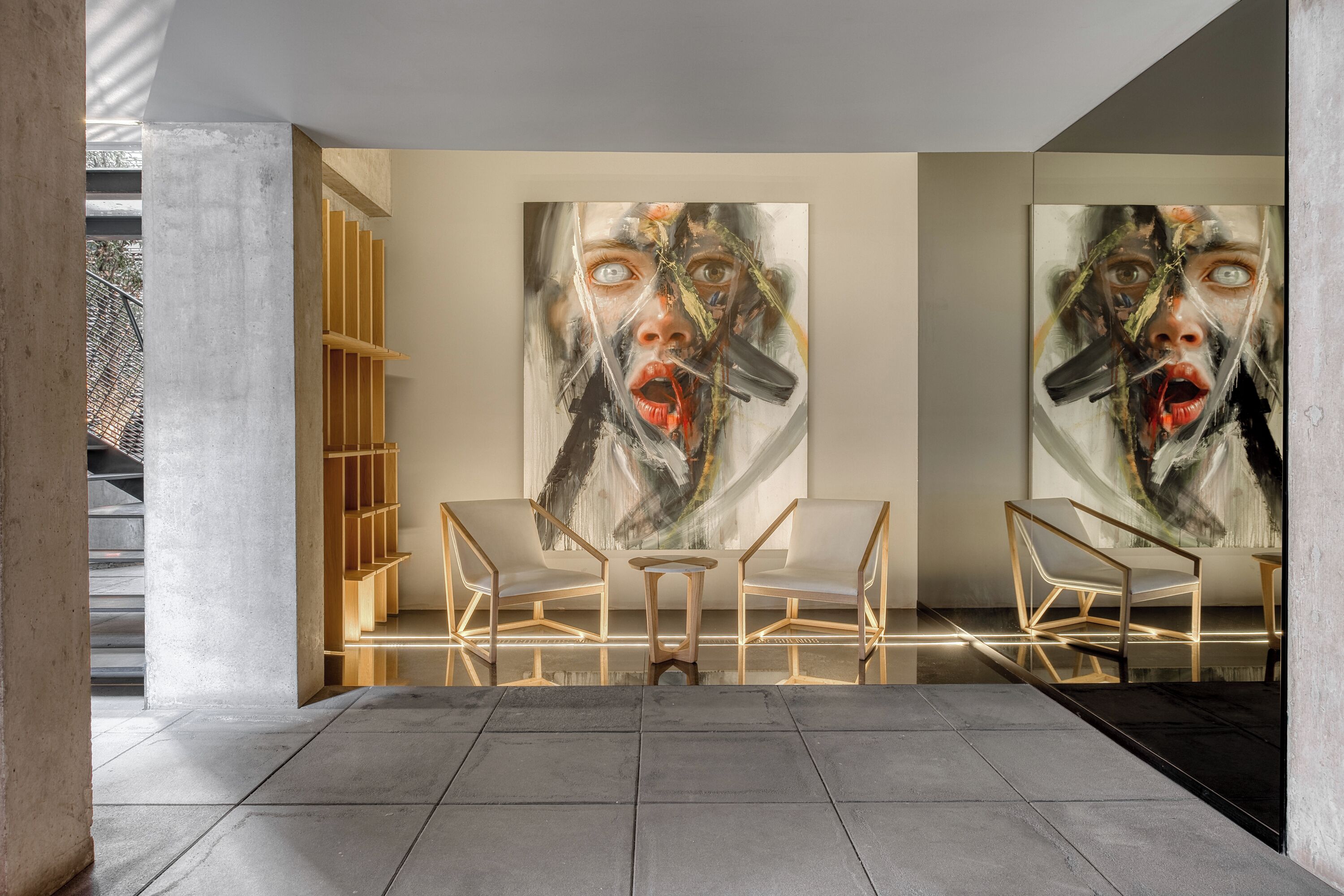 Ein modernes Interieur mit minimalistischem Design, das eine Sitzecke mit zwei Stühlen und einem kleinen Tisch sowie großformatige abstrakte Gemälde an den Wänden zeigt.