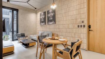 A modern interior with a round wooden table, grey sofa, and wooden chairs. There are two wall-mounted artworks and a wooden door.