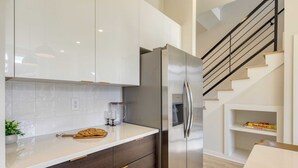 Une cuisine moderne avec un réfrigérateur en acier inoxydable, des armoires blanches et un plan de travail en bois.