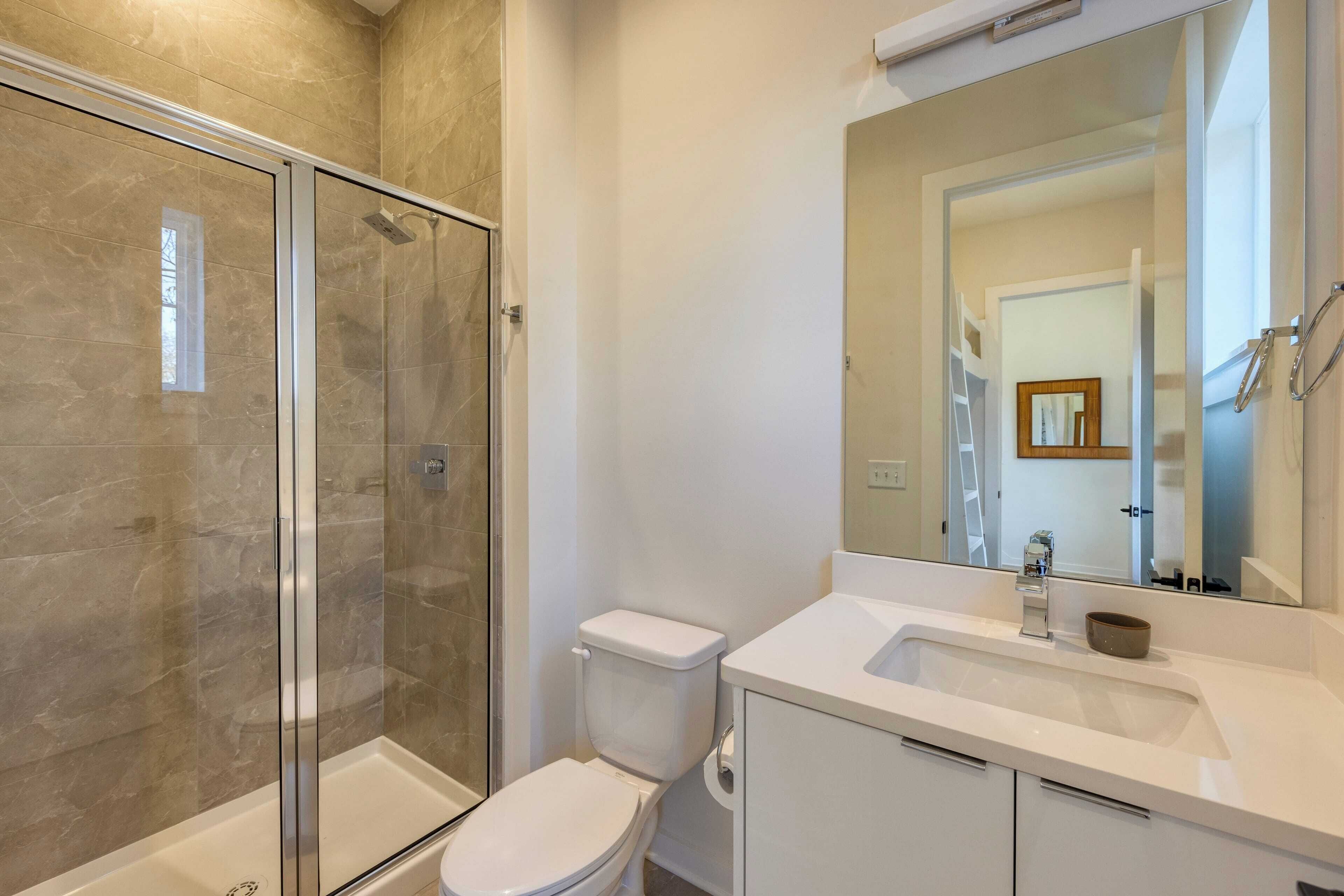 Une salle de bain avec une douche à parois de verre, des toilettes blanches et un lavabo avec un miroir au-dessus.