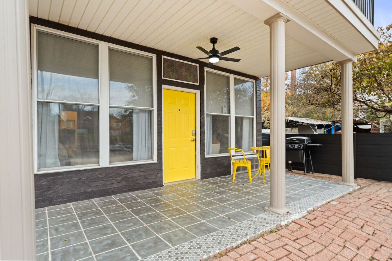 Una casa con una porta gialla, ampie finestre, un portico coperto e un patio con sedie.
