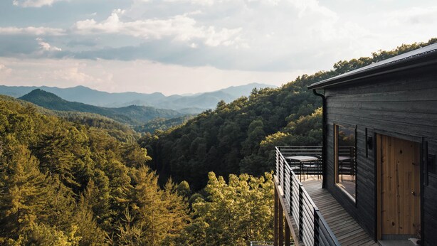 Een houten chalet met balkon, uitzicht op een bebost dal en verre bergen.