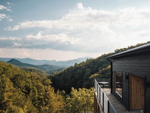 A wooden cabin with a balcony overlooking a forested valley and distant mountains. - Long View Resort (Bryson City)