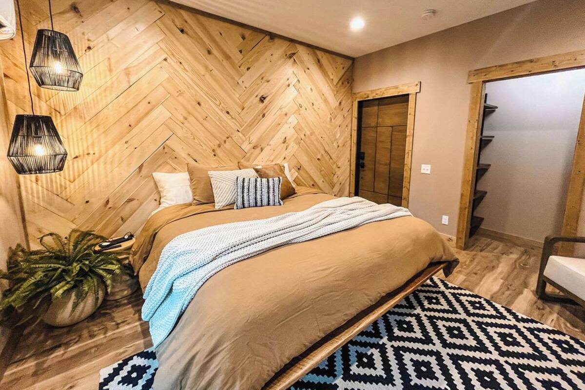 Un dormitorio con pared de madera con motivo de espinilla, una cama grande con alfombra estampada y una planta en maceta.