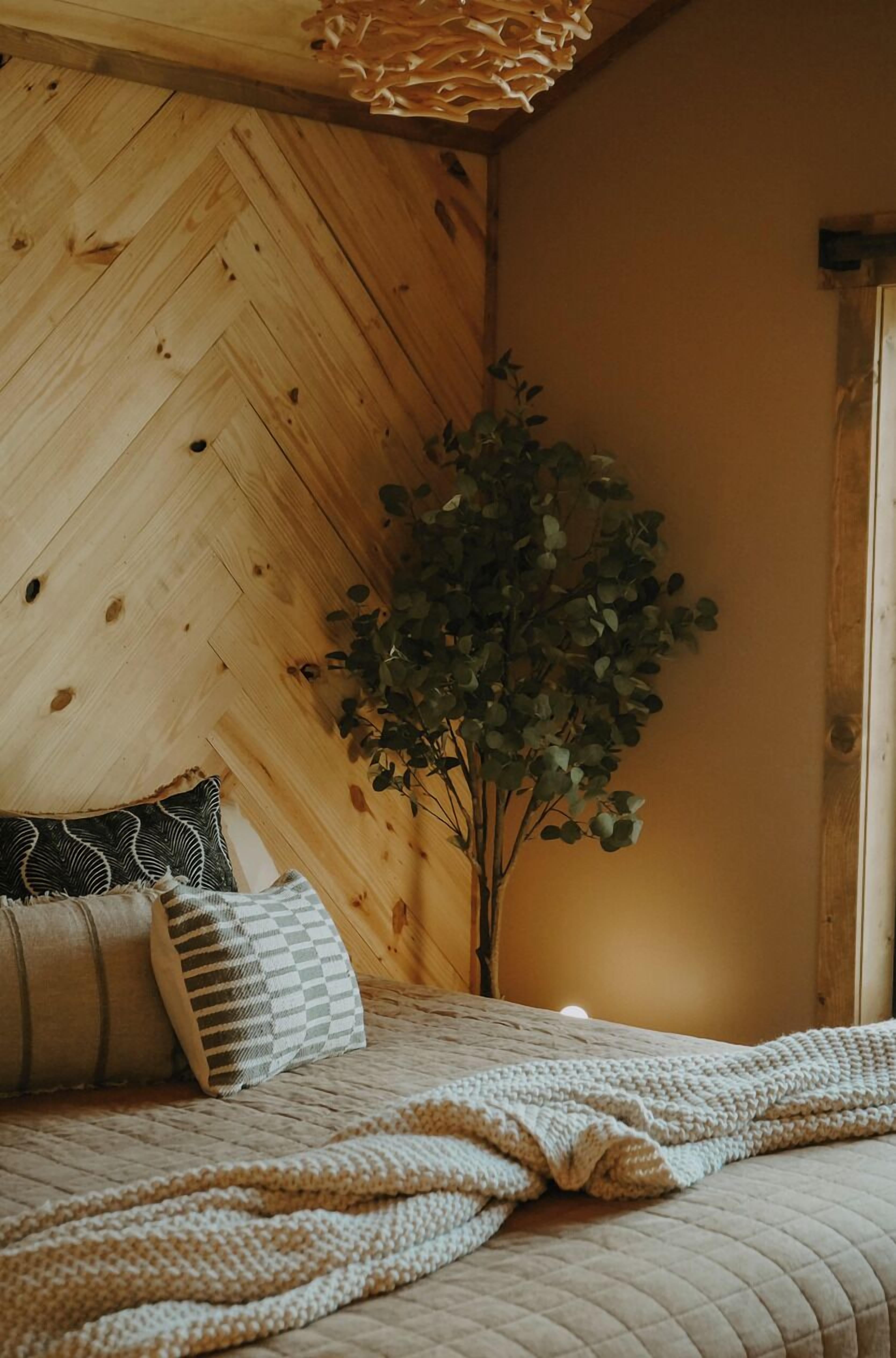 Un dormitorio acogedor con techo de madera, un ventanal grande y una planta.