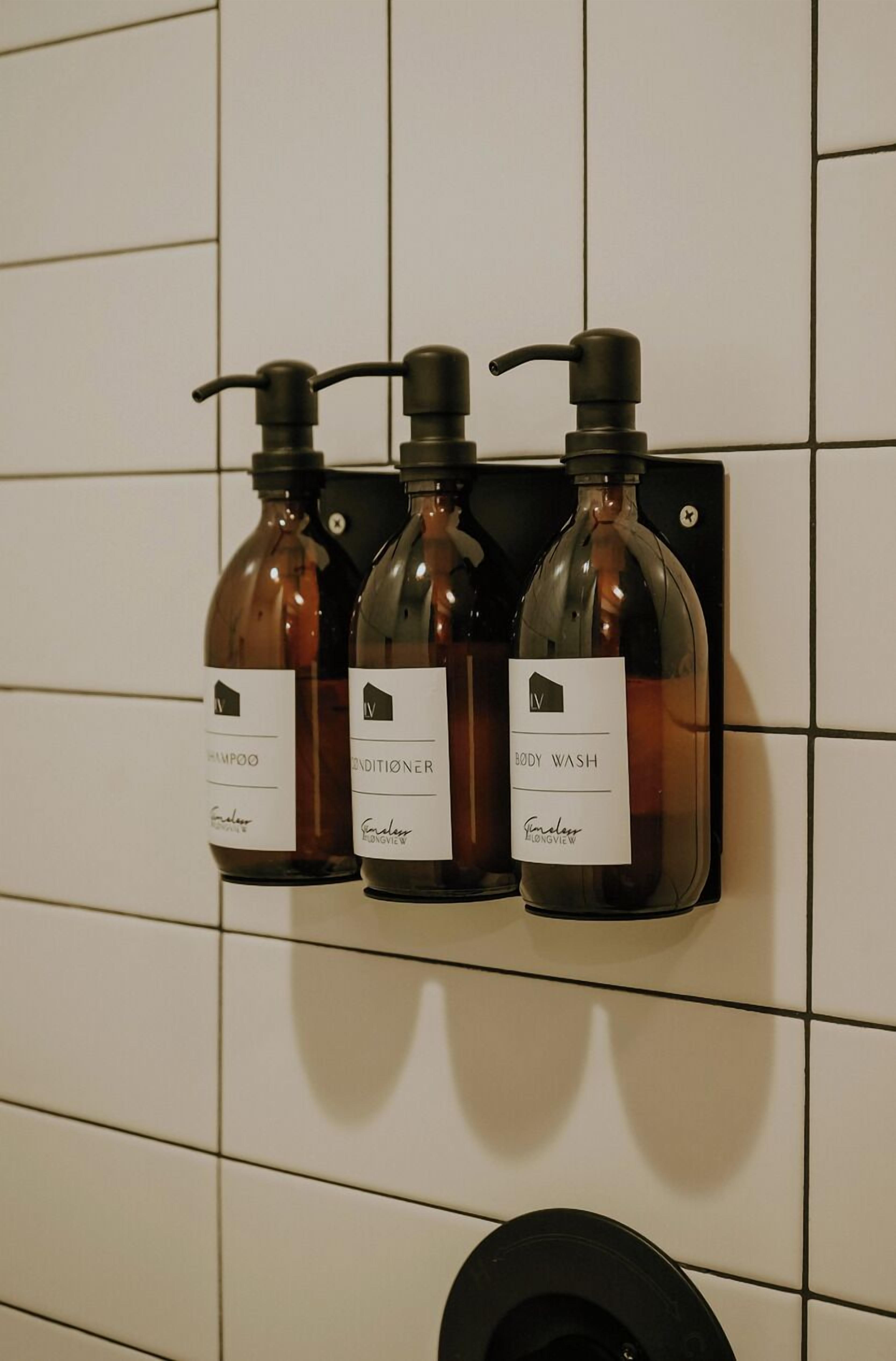 Three bottles of body wash, shampoo, and conditioner on a wall-mounted dispenser in a bathroom.