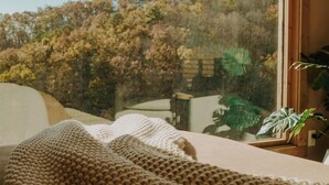Een kamer met een groot raam, uitzicht op bomen en een gebreide deken op het bed.