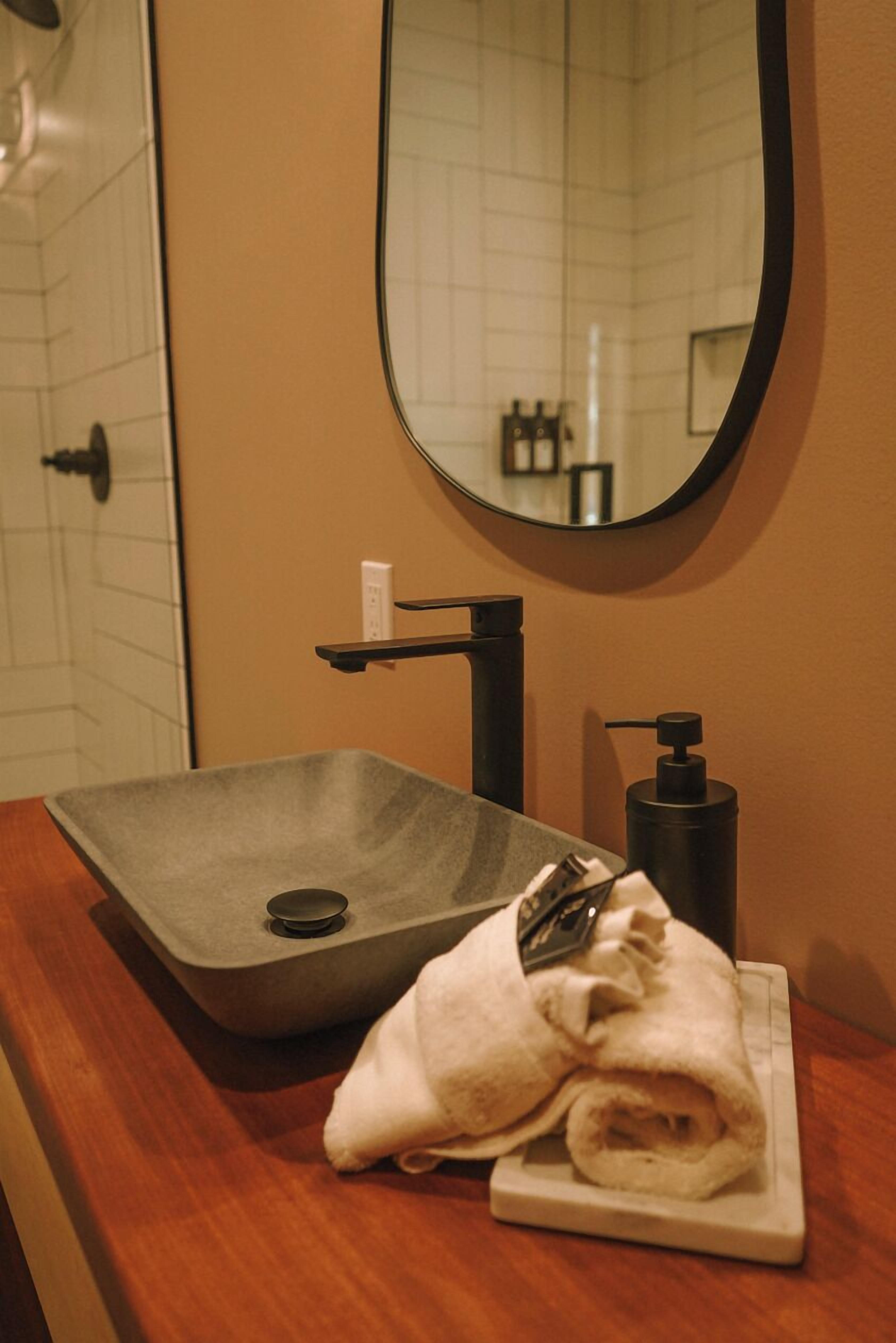 A bathroom with a rectangular sink, a mirror, and a towel on a tray.