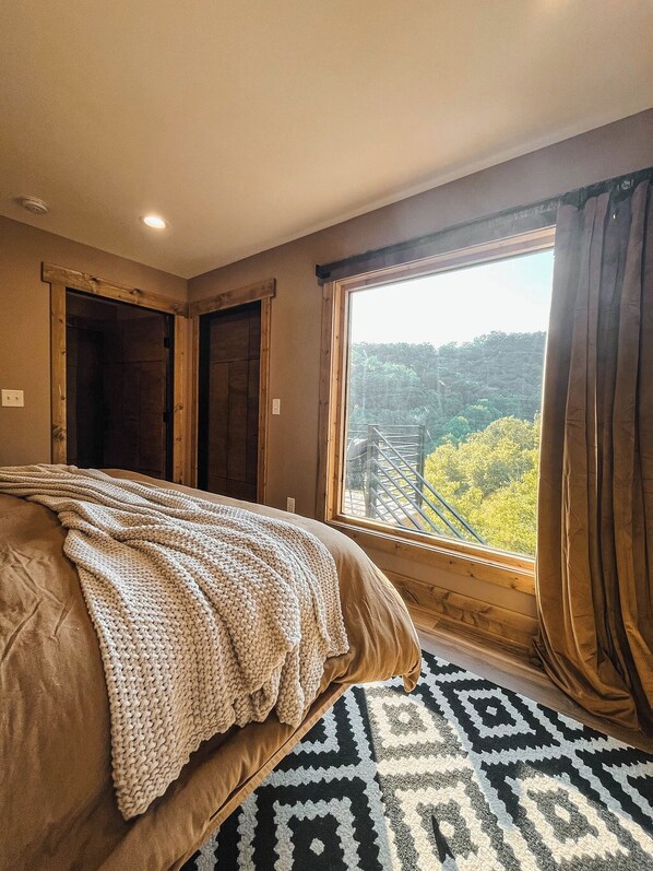 Une chambre avec un grand lit, une vue sur une forêt par la fenêtre et un tapis à motifs.