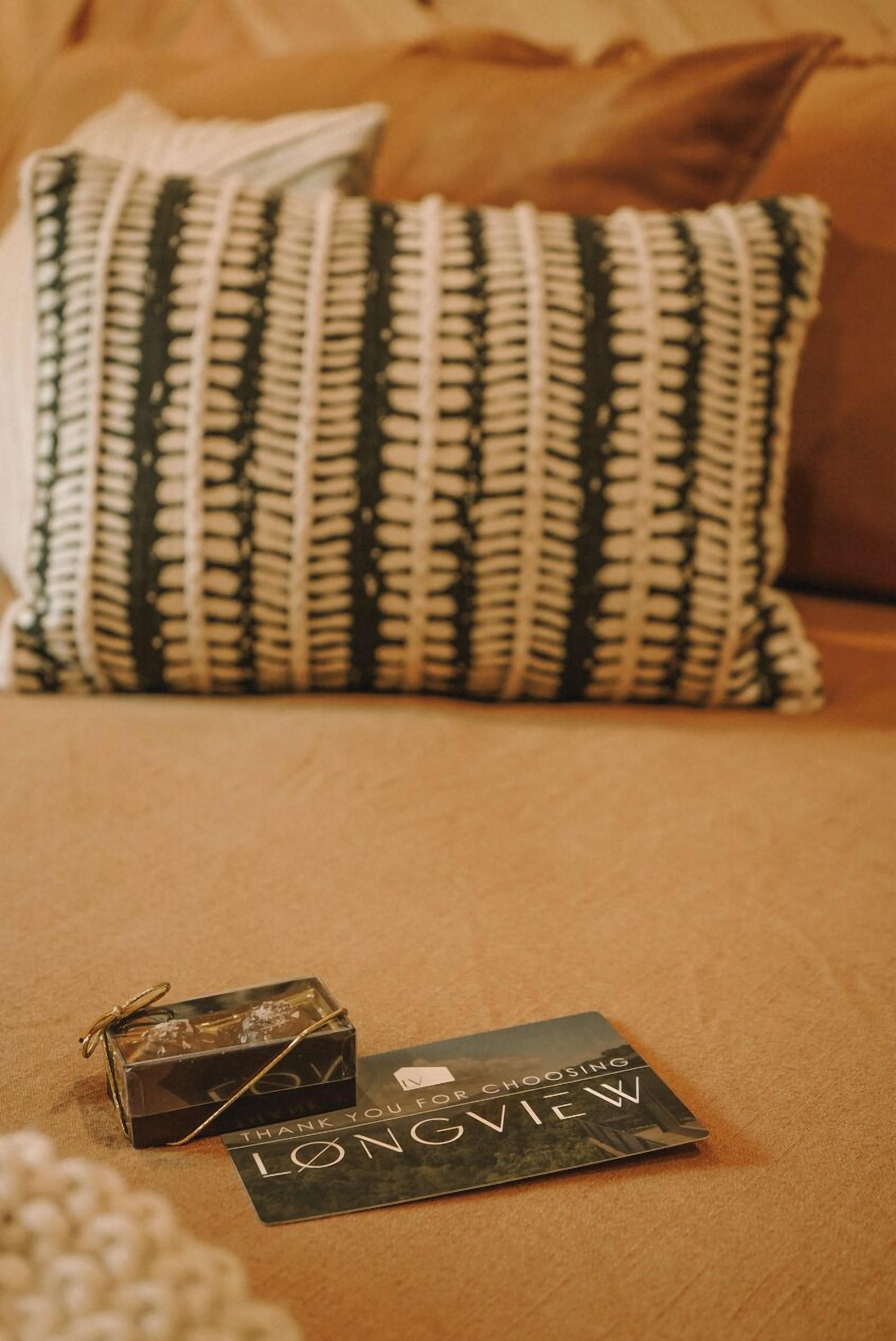 Un lit avec un oreiller à motifs, une carte de remerciement et une petite boîte cadeau.