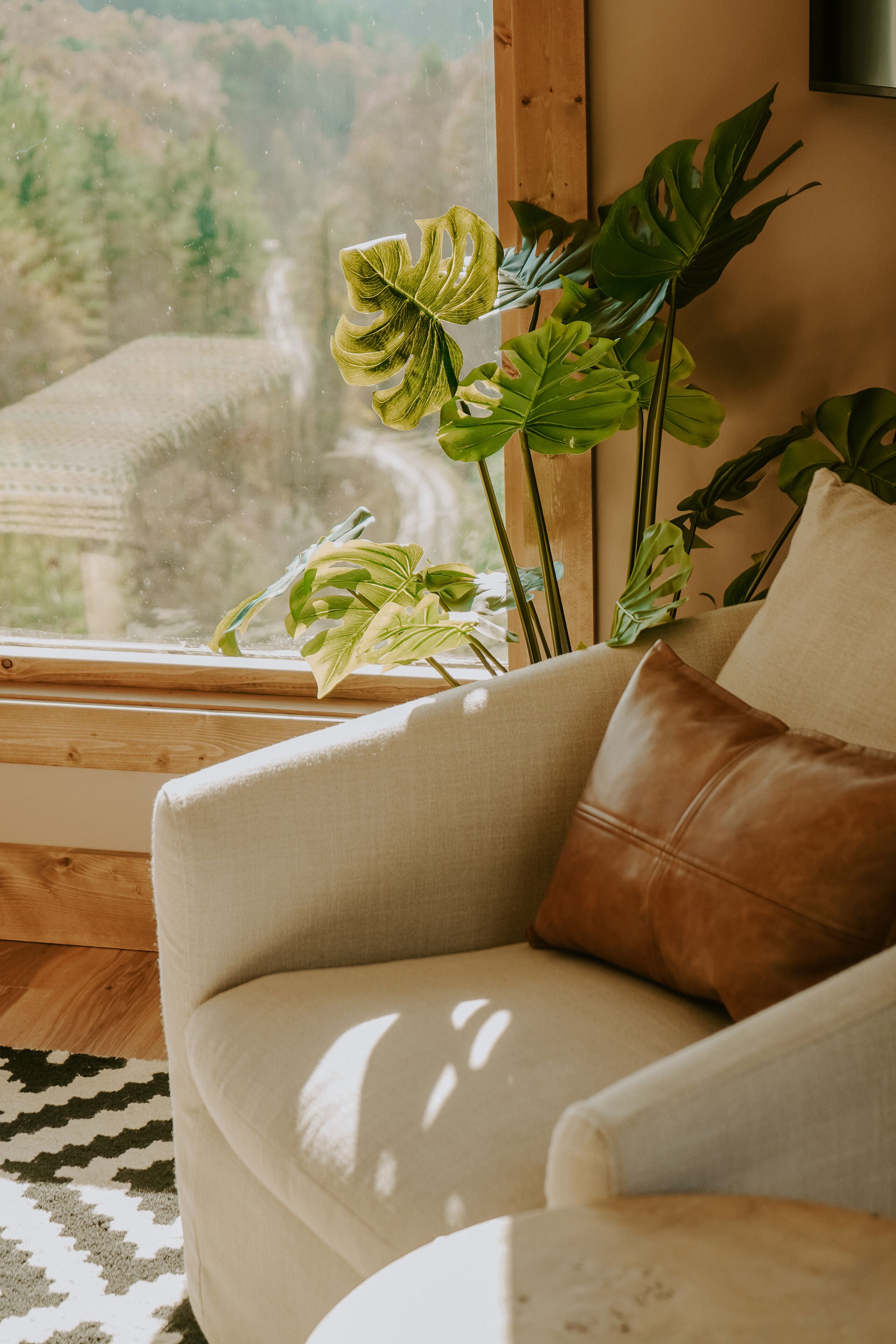 Une pièce confortable avec un fauteuil moelleux, une grande fenêtre donnant sur une forêt et une plante en pot.