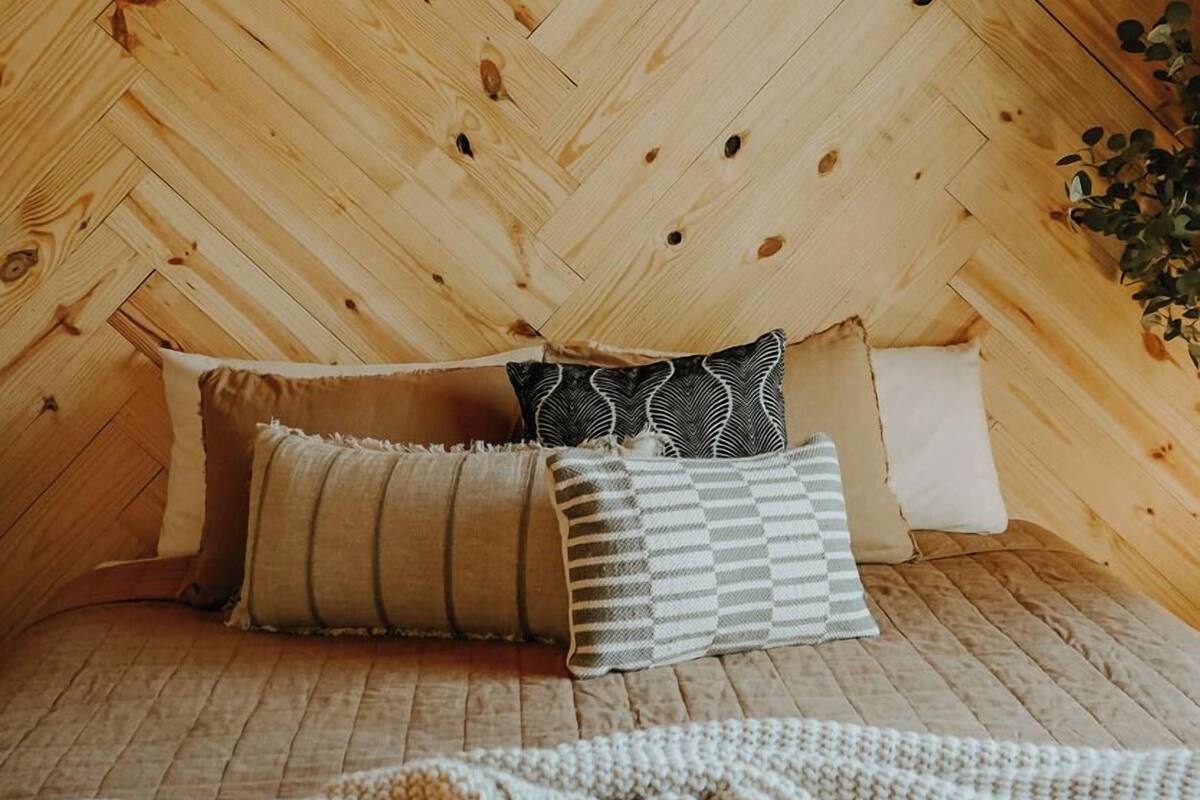 Una habitación acogedora con techo de madera con motivo de espiga, una cama con manta de punto y dos almohadas.