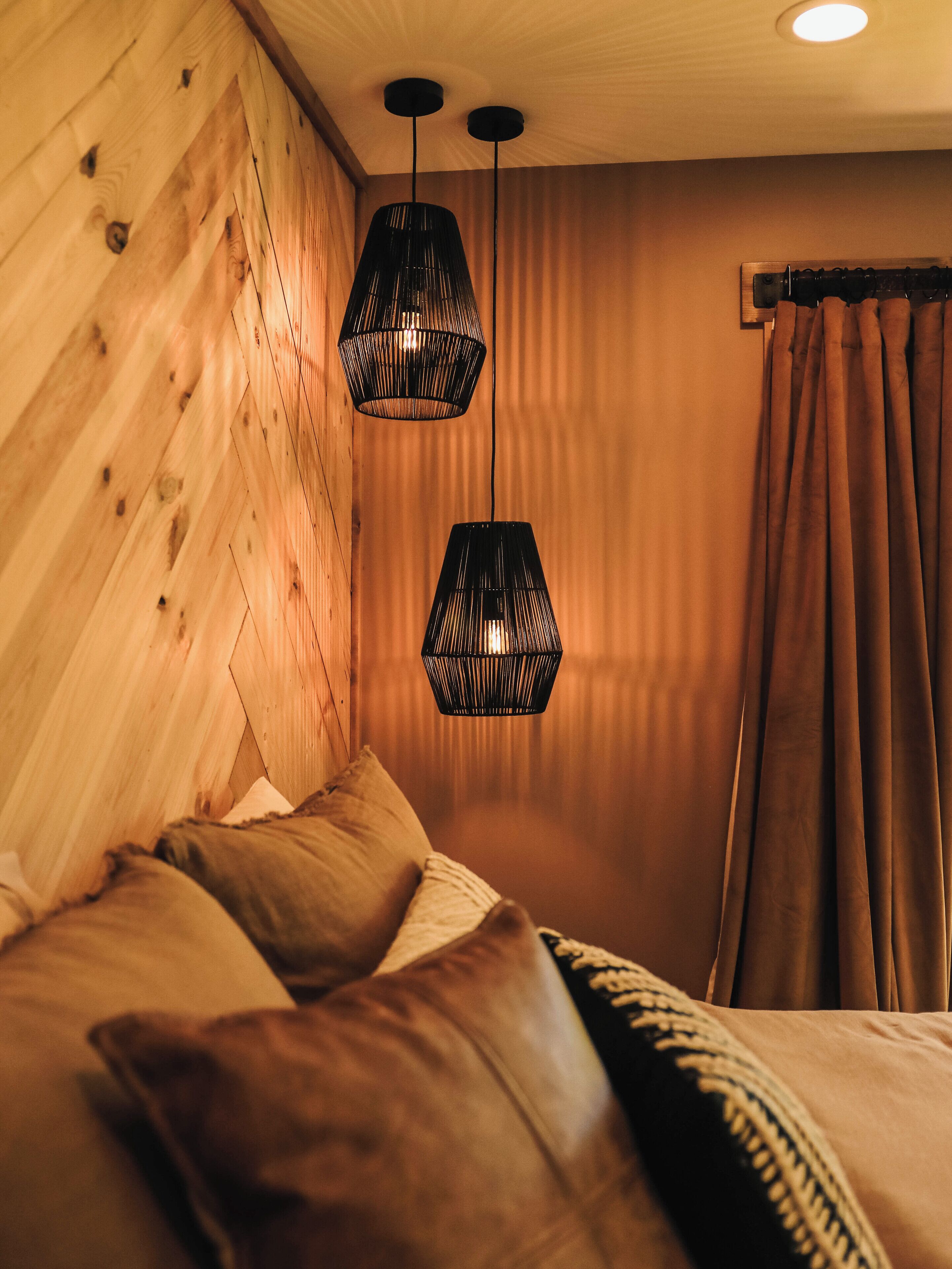 A bedroom with wooden walls, a bed with brown bedding, and two hanging black lamps.