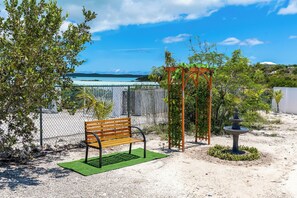 A bench with a green mat, a pergola with vines, and a fountain in a garden with a view of the sea.
