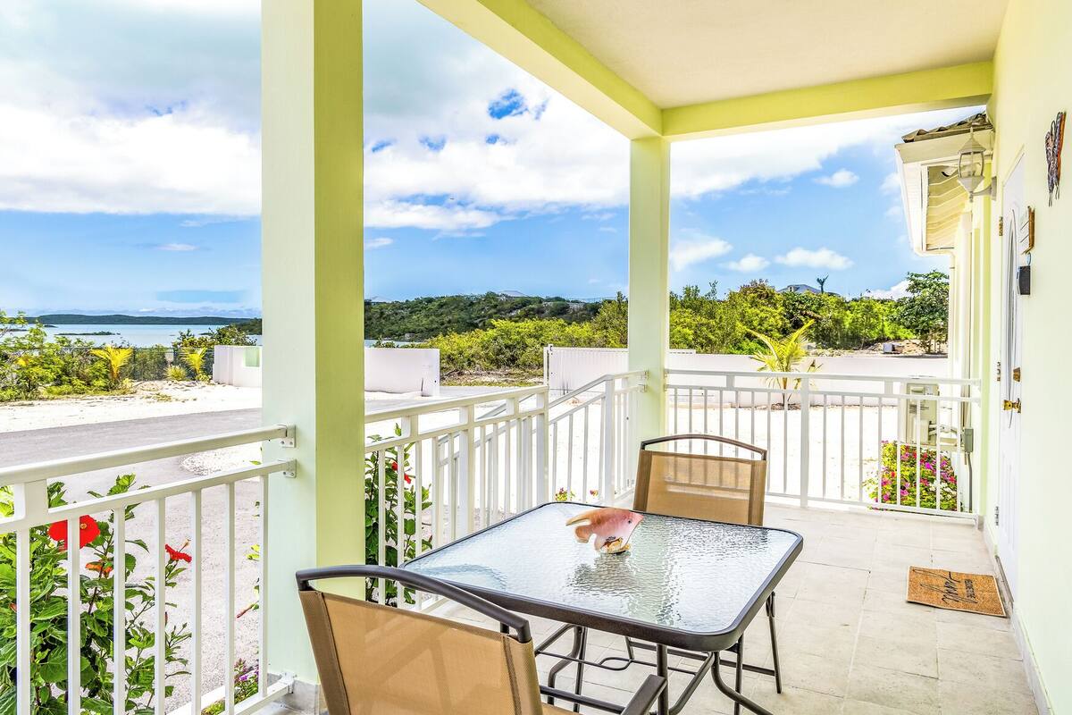 Un balcon avec une table et des chaises, offrant une vue panoramique sur la mer et la verdure.