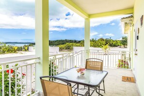 A balcony with a table and chairs, overlooking a scenic view of the sea and greenery.