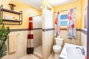 A bathroom with a shower, toilet, sink, and decorative elements like a towel rack and a plant.
