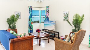 Una sala de estar acogedora con televisor, mobiliario de mimbre y vista al mar a través de una ventana.