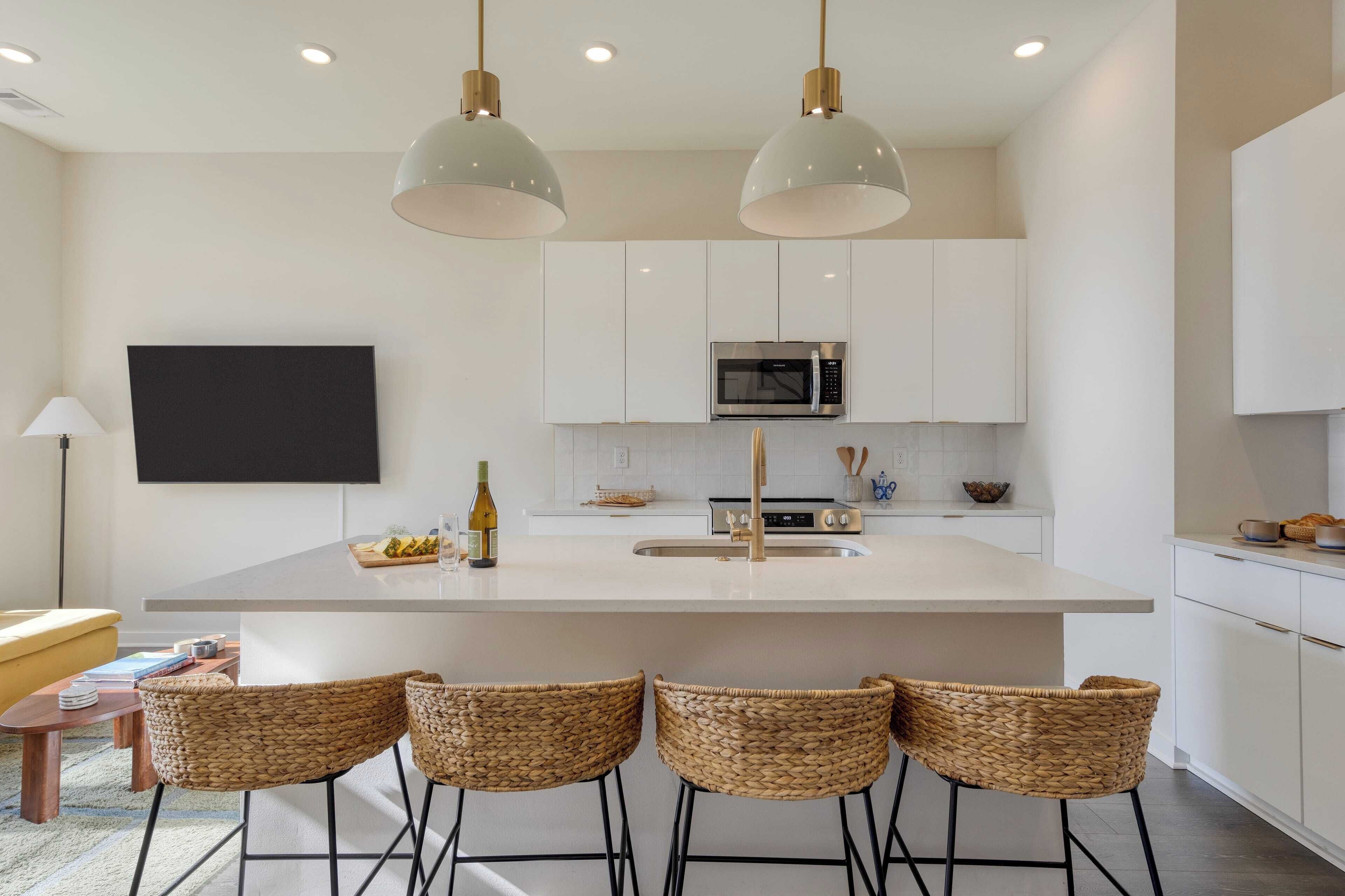 A modern kitchen with white cabinets, a central island with bar stools, a microwave, and a large window.