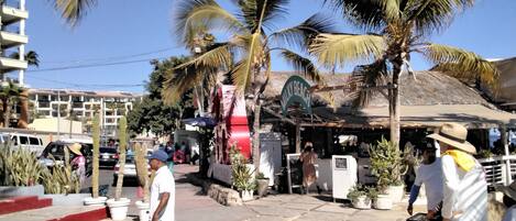 Cena de rua com um edifício com a placa 'NILIY BEACH' e palmeiras.