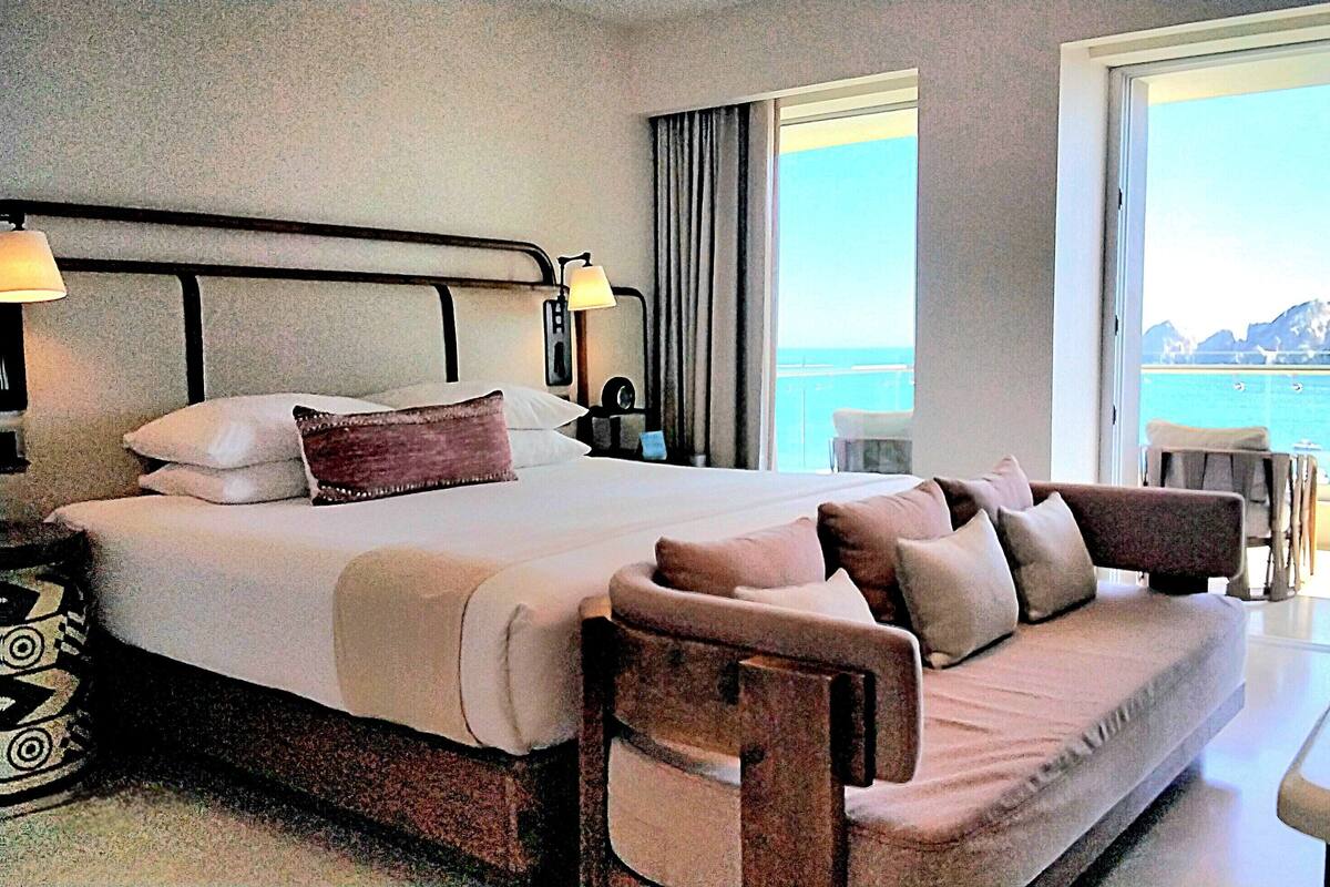 A hotel room with a large bed, a sofa, a desk, and a view of the sea.
