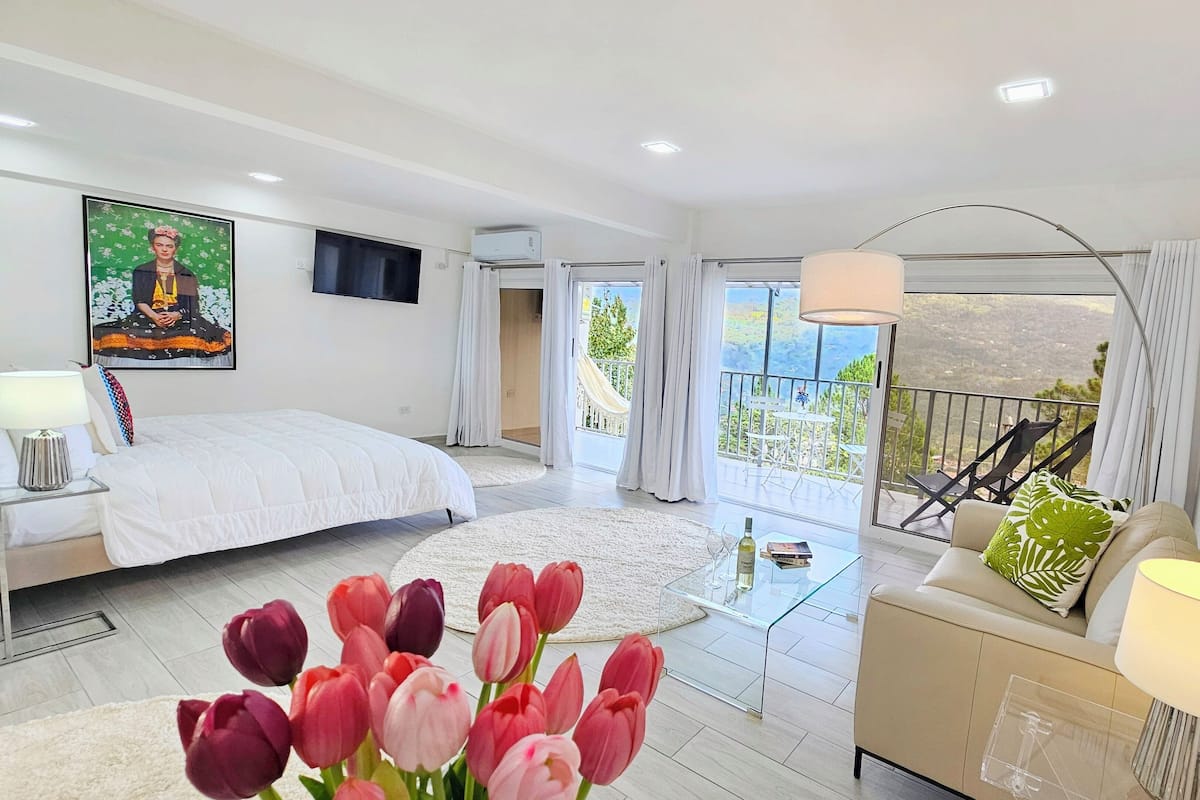A modern bedroom with a large bed, a balcony with a view, and a painting on the wall.