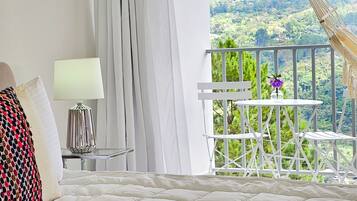 A bedroom with a bed, a bedside table with a lamp, and a view of a balcony with a table and chairs.