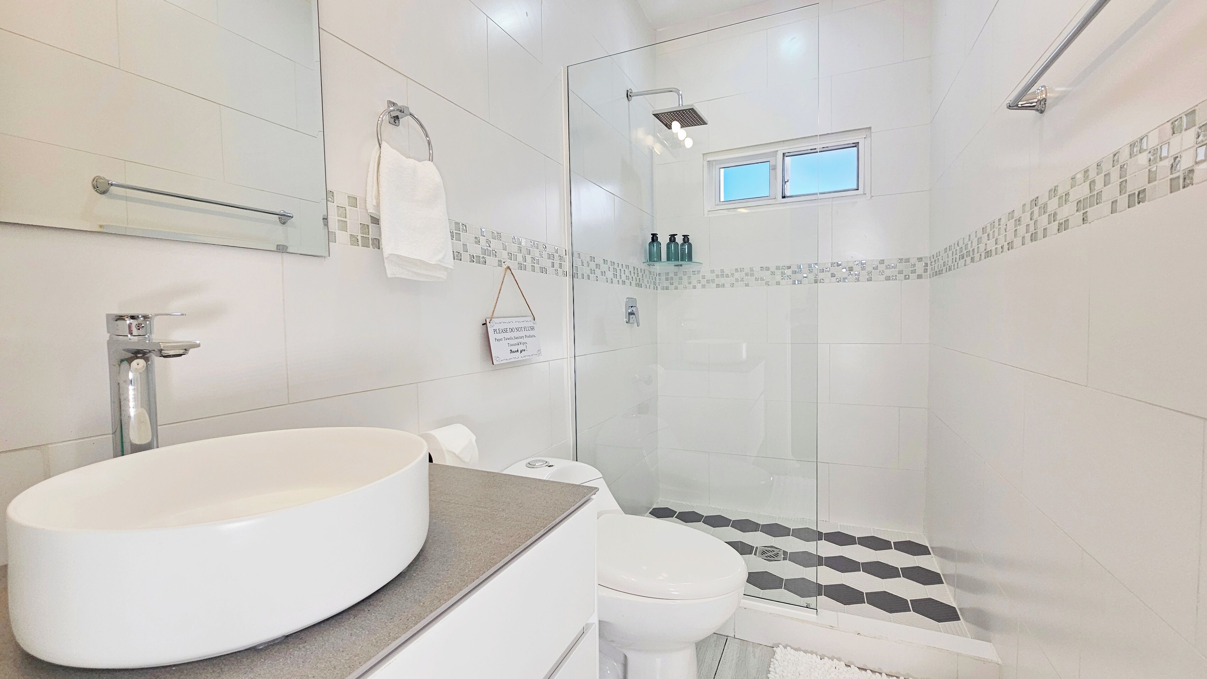 Une salle de bain moderne avec un grand lavabo blanc, des toilettes et une douche séparée par une paroi de verre.