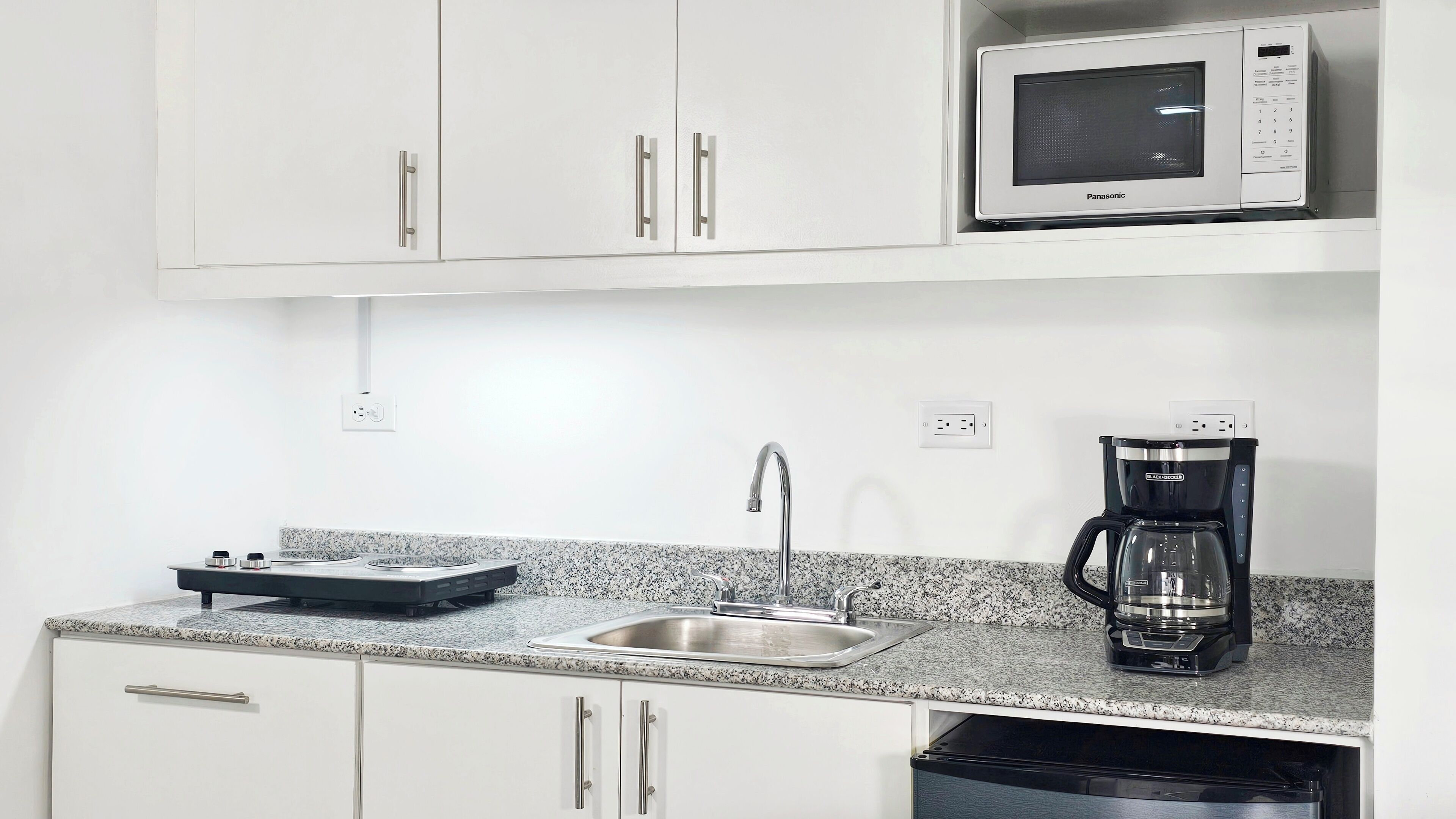 A kitchen with white cabinets, a microwave, a coffee maker, and a sink.