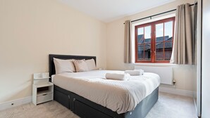 Una cama bien hecha con sábanas blancas, cabecera negra y una mesita de noche blanca con repisa.