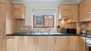 Cocina moderna con armarios de madera, encimera negra, ventana con vistas a edificios y un tostador.