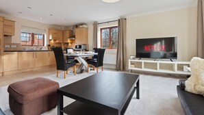 Una sala moderna con un televisor de pantalla plana, un comedor con mesa y sillas, y una cocina al fondo.