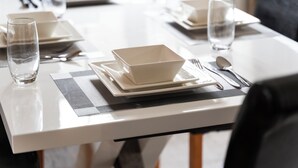 Una mesa de comedor bien dispuesta, con mantel blanco, vasos transparentes, cubiertos y un bol sobre un camino de mesa.