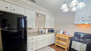 Cucina con mobili bianchi, frigorifero nero, microonde, piano cottura ed un ripiano in legno.