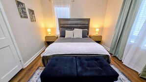 Una camera da letto con un letto, due lampade da comodino, una finestra con persiane, un tappeto decorato e una porta.