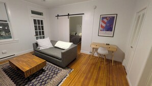 Ett modernt vardagsrum med en grå soffa, ett soffbord i trä, ett litet skrivbord med en stol och en mönstrad matta.