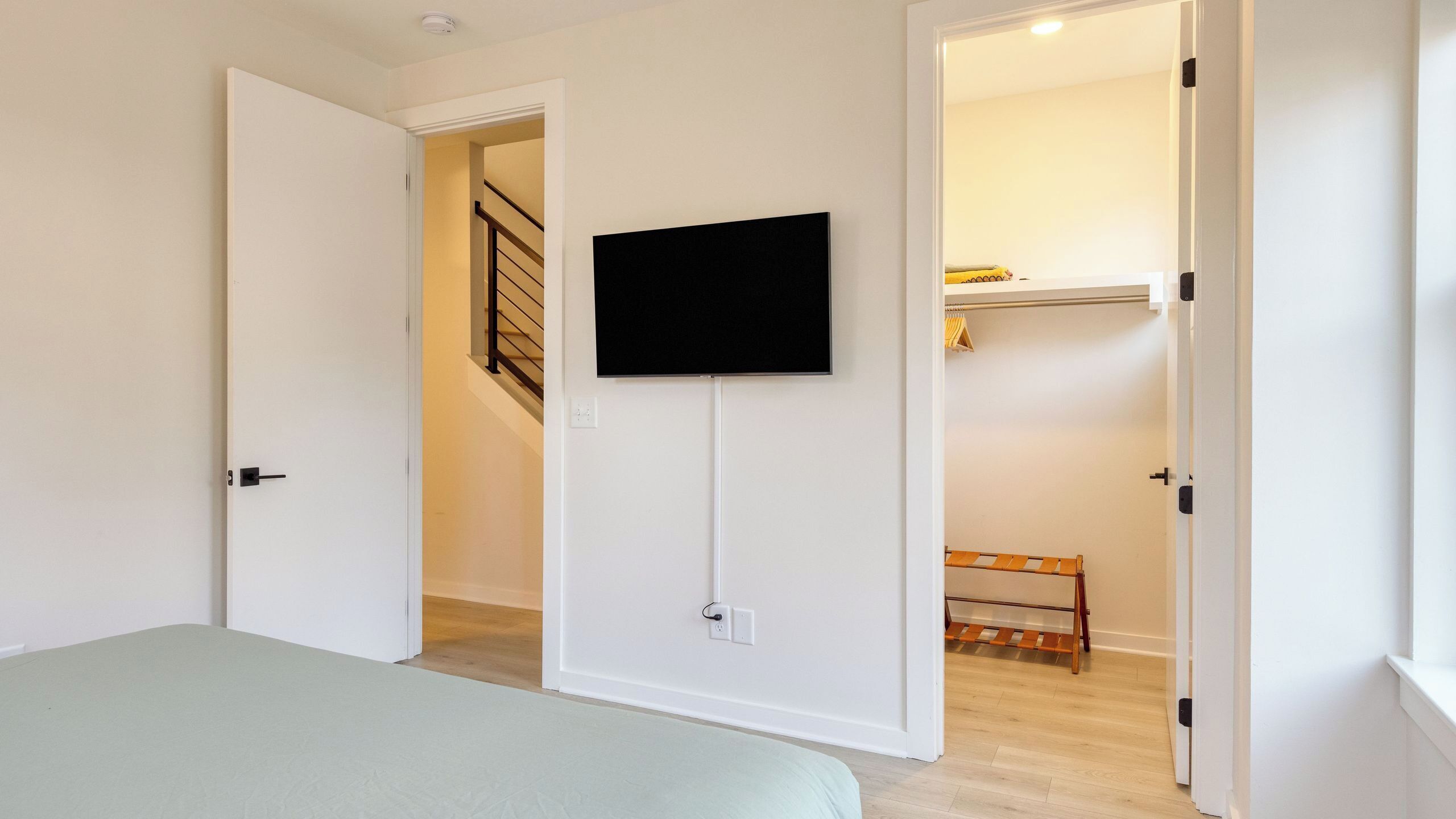 Quarto com cama, televisão na parede e escada para outro cômodo.