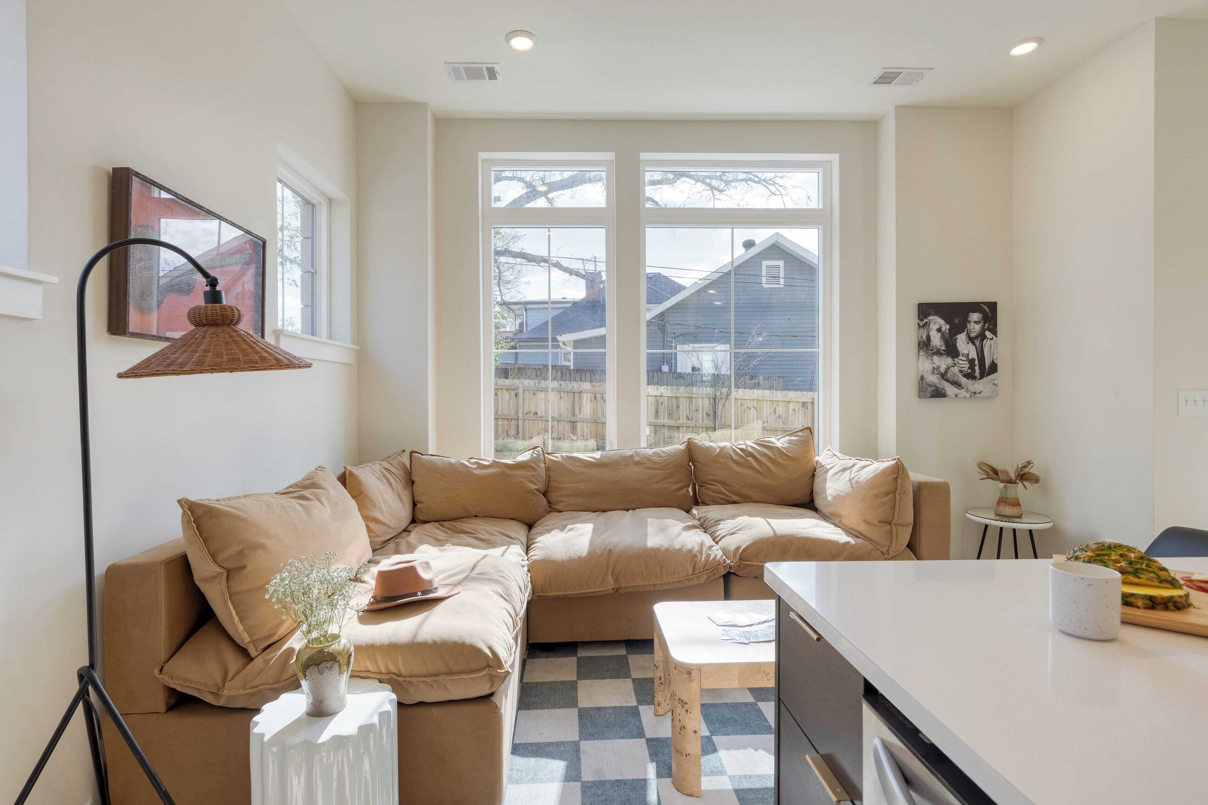 A modern living room with a beige sectional sofa, a small white table, and a kitchen area with a white countertop.