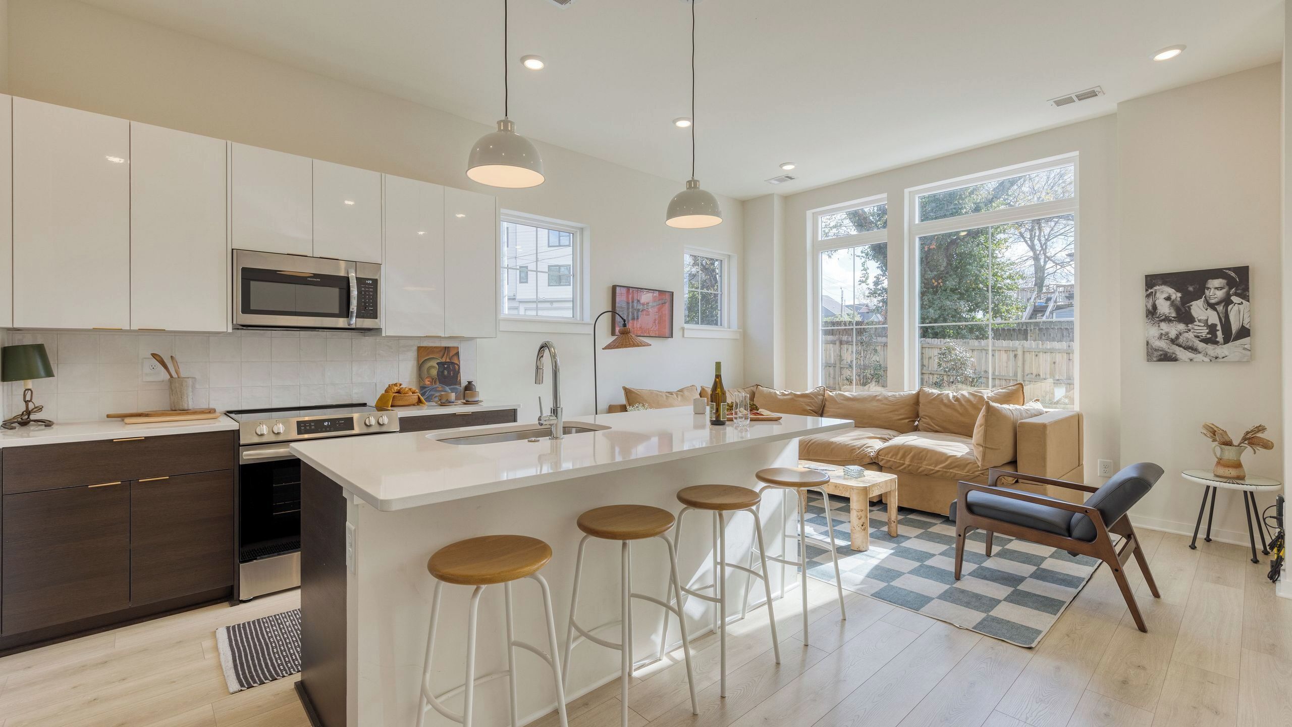 A modern kitchen with white cabinets, a central island with stools, a dining area with a sofa, and large windows.