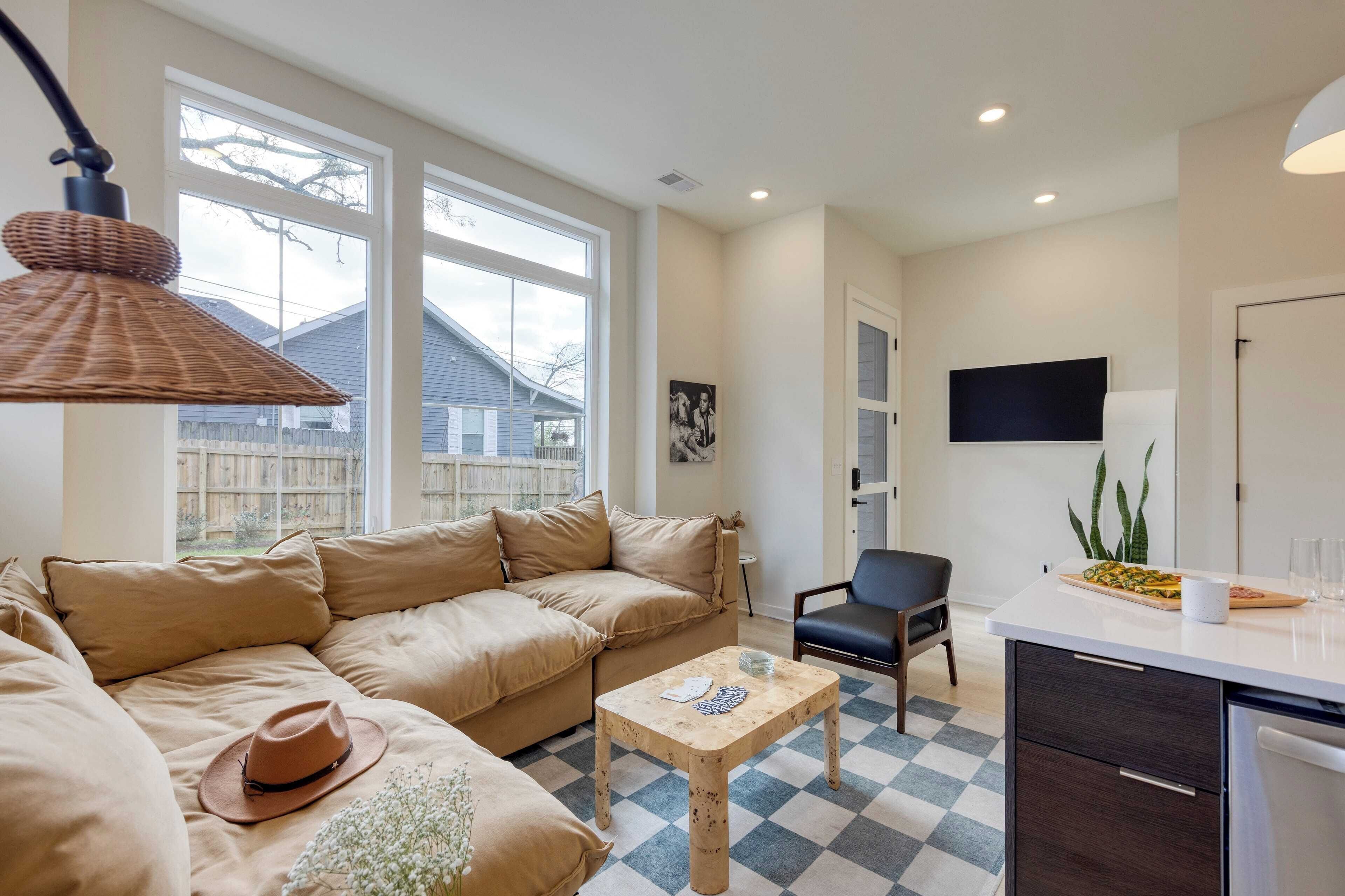 A modern living room with a beige sofa, a coffee table, and a dining area with a TV and a plant.