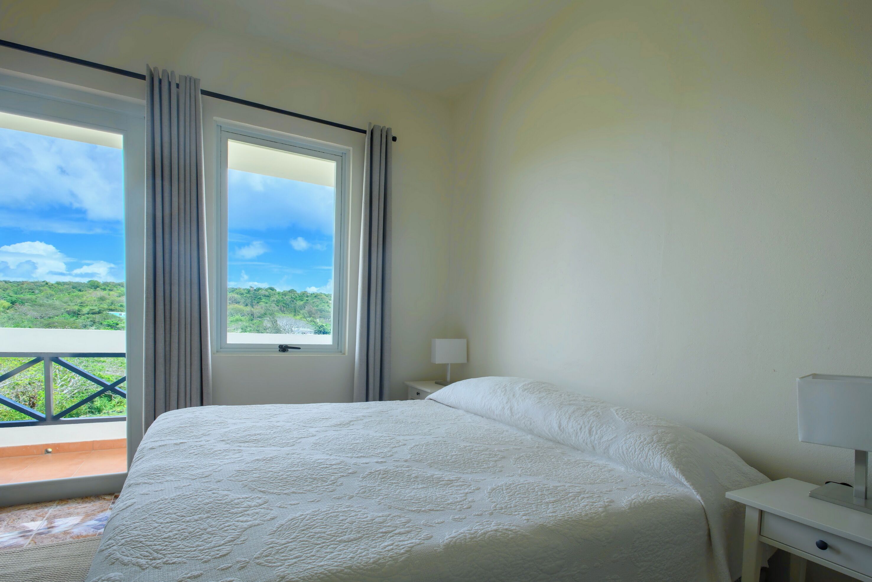 A bedroom with a large bed, a nightstand with a lamp, and a window with curtains.