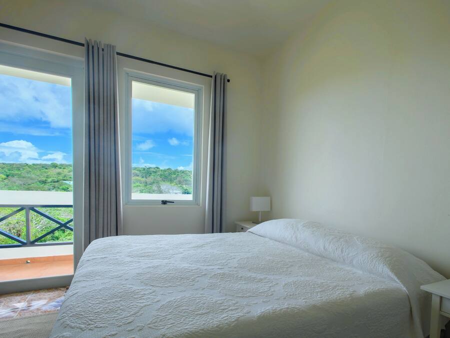 A bedroom with a large bed, a nightstand with a lamp, and a window with curtains.
