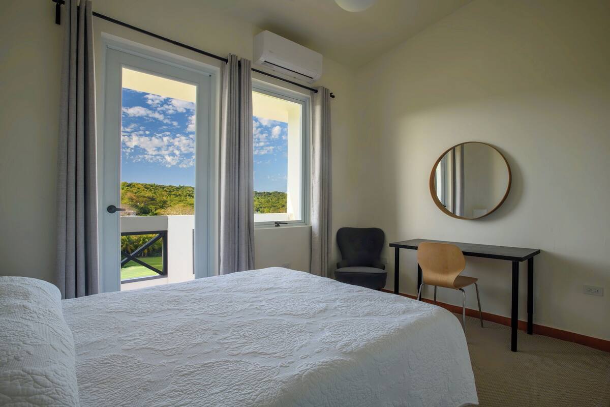 A hotel room with a bed, a desk, a chair, and a balcony with a view of the landscape.